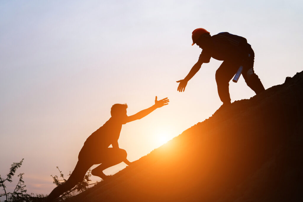 Two individuals supporting and assisting each other on a mountain at sunset in their journey to help ex-offenders find employment opportunities.