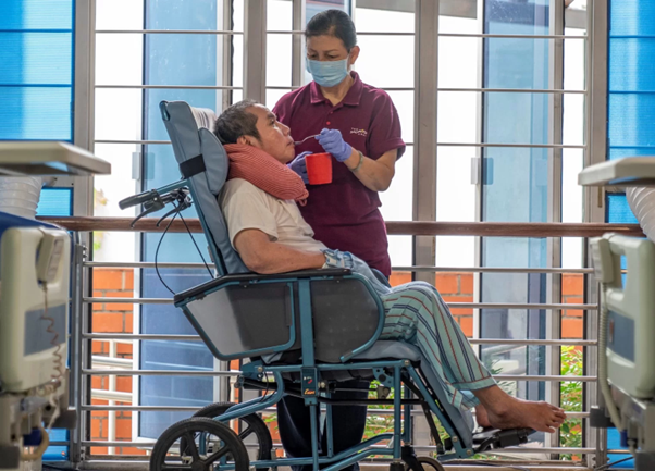 A woman is providing nursing care for a man with dementia  in a wheelchair